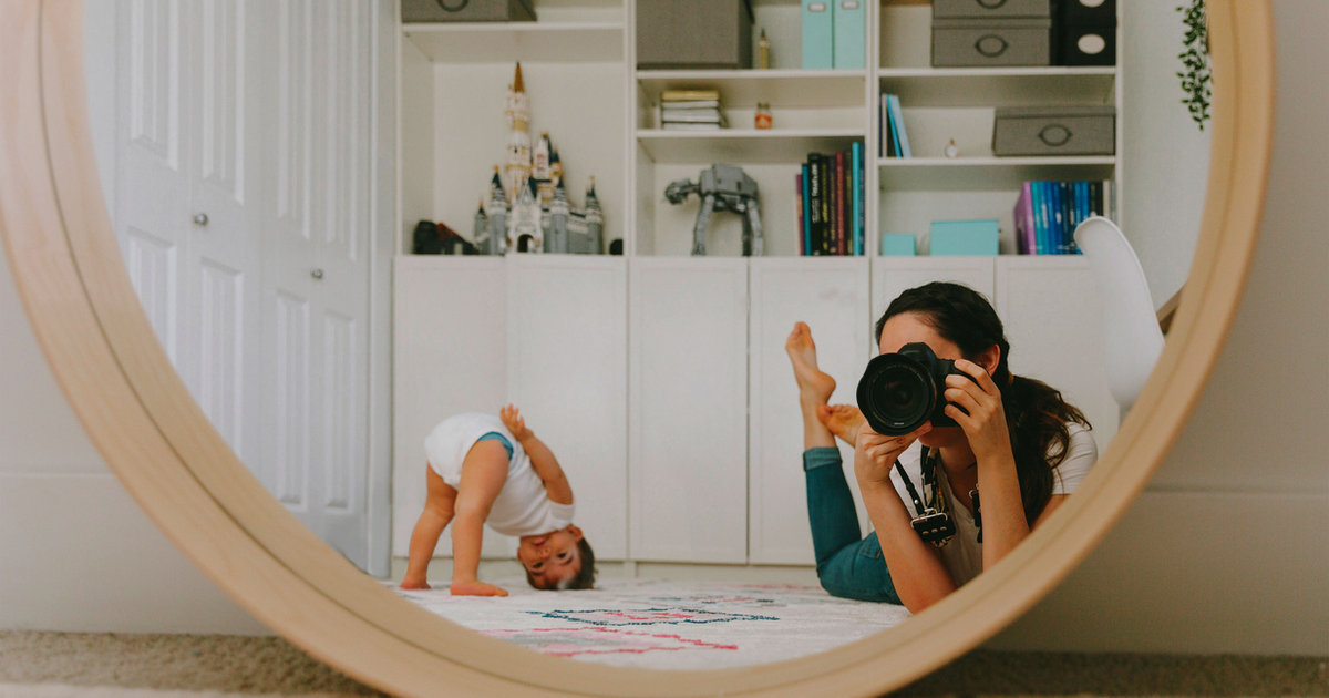 A woman lying down, reflected in a large round mirror in a bright room.