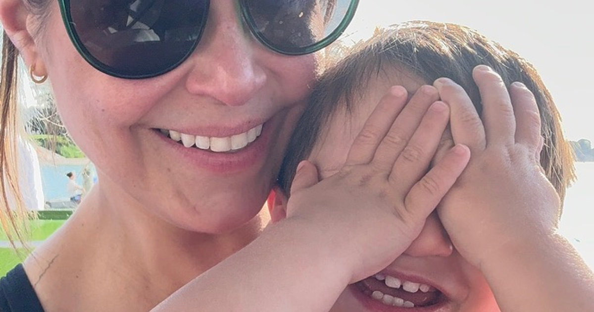 A smiling mom in sunglasses with her young child playfully covering his eyes.