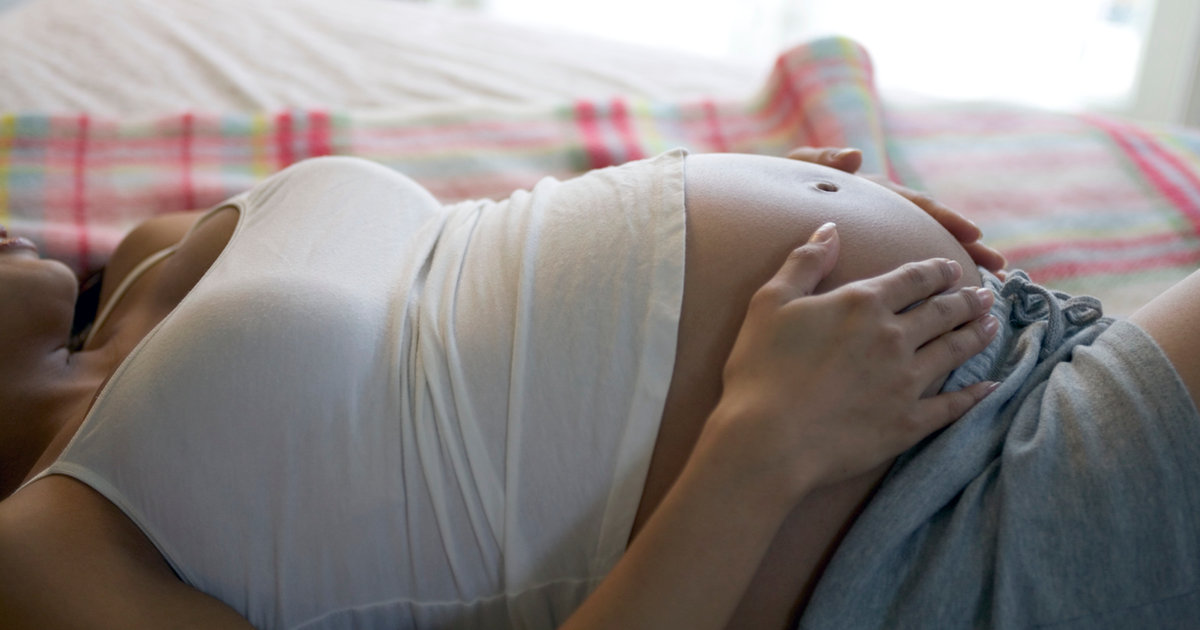 A pregnant woman resting, cradling her belly with both hands.