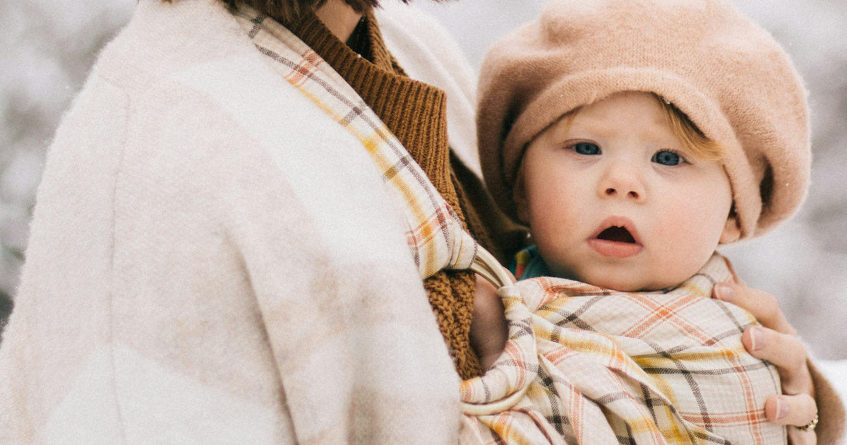A mother holding her baby, who is wrapped in a knit beret and blanket.