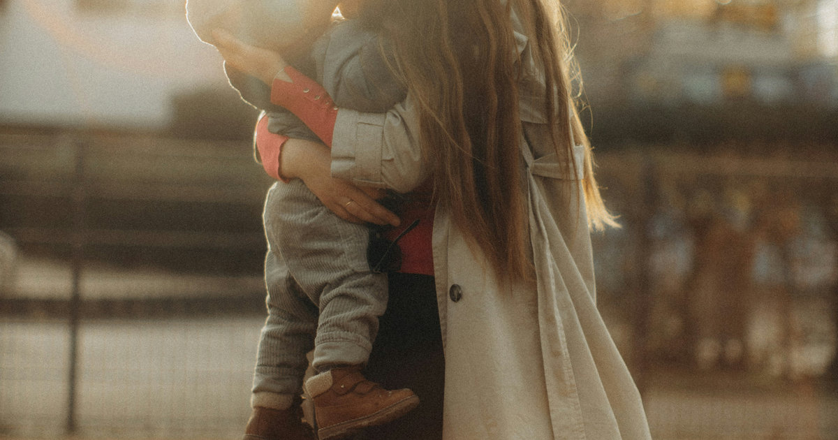 A mother holding her child close in warm, golden evening light.